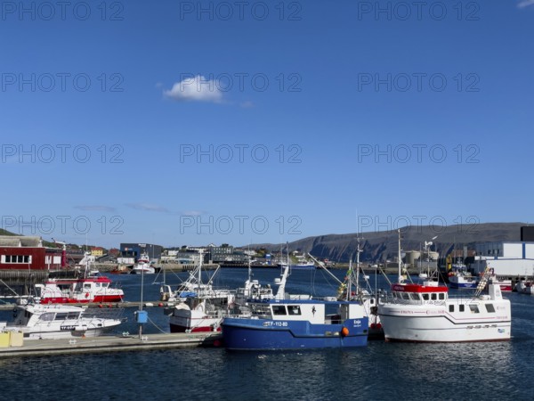 Several fishing boats in Batsfjord harbour, blue sky, mountains in the background, sunny day,