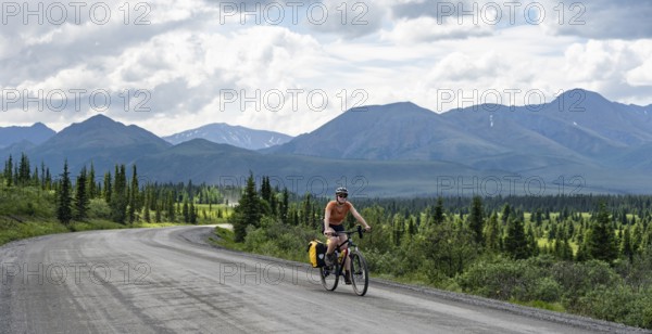 Young woman riding a bicycle on a dirt road through the tundra, mountainous landscape, Denali Park