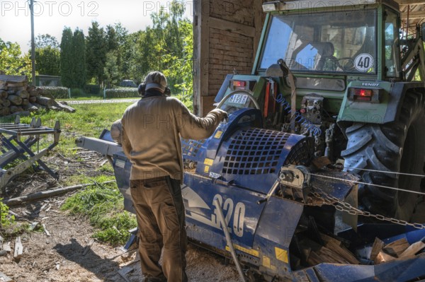 Young man sawing and splitting beech logs with his saw cutting machine, powered by a tractor in a