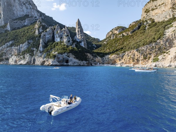 Motor boat off picturesque rocky coast, cliffs with L'Aguglia pinnacle, blue sea and Cala Goloritzé