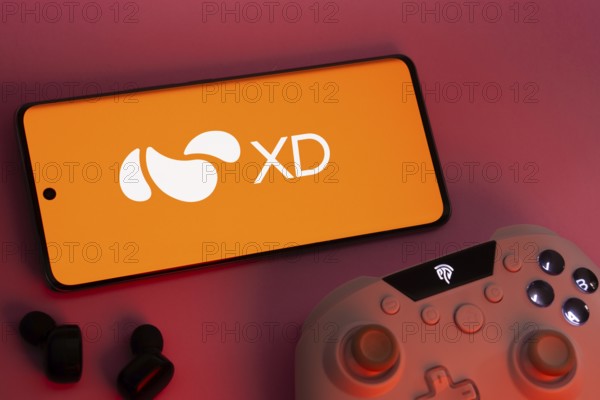 Dhaka, Bangladesh- 22 Mar 2025: Smartphone with XD logo, game controller, and earbuds on a pink