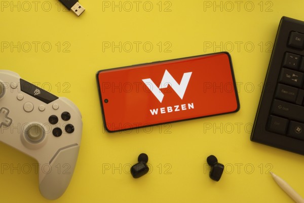 Dhaka, Bangladesh- 22 Mar 2025: Smartphone with Webzen logo, game controller, and earbuds on a