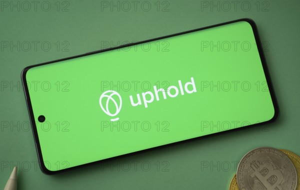 Dhaka, Bangladesh- 19 Sep 2025: Uphold logo on smartphone screen near Bitcoin coin and QR code on