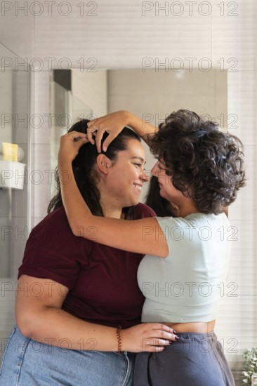 A lesbian couple shares a morning routine in the bathroom, styling hair, creating a candid and
