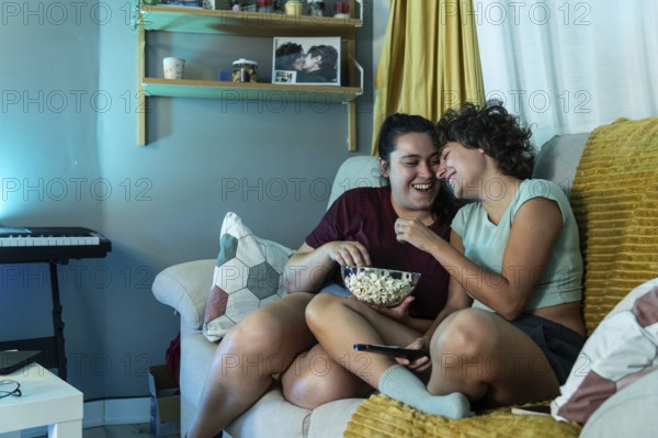 A joyful lesbian couple eating popcorn while watch tv, highlighting domestic harmony and love