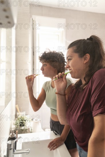 A lesbian couple shares a morning routine in the bathroom, with one applying makeup and the other