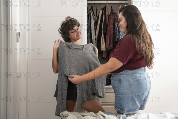 A joyful lesbian couple shares a moment while picking out clothes. One holds up a gray sweater,