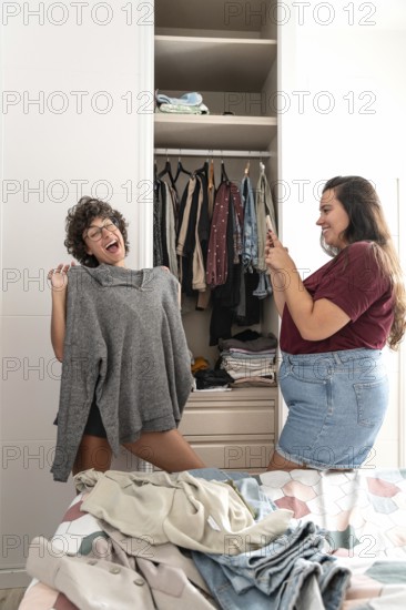 A joyful lesbian couple shares a moment while picking out clothes. One holds up a gray sweater,