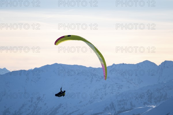 Paragliders flying over snowy mountain peaks in winter in evening light, Kitzbühel Alps, Tyrol,