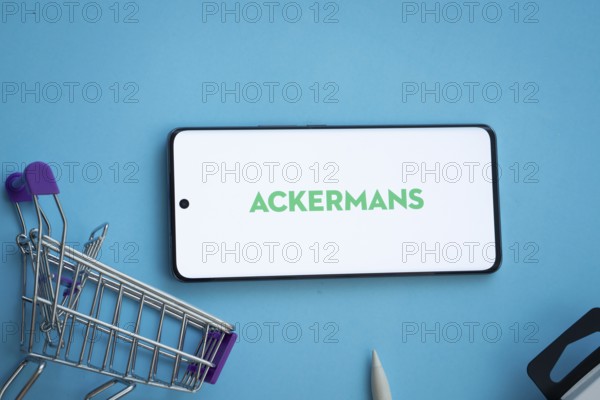 Dhaka, Bangladesh- 03 July 2025: Smartphone displaying Ackermans logo with shopping cart on a blue