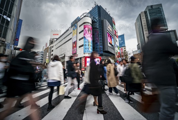 Crowd crossing zebra crossing on a large intersection, motion blur, back modern houses with