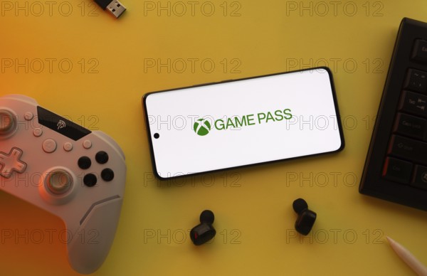 Dhaka, Bangladesh- 15 July 2025: Smartphone with Xbox game pass logo, game controller, and earbuds