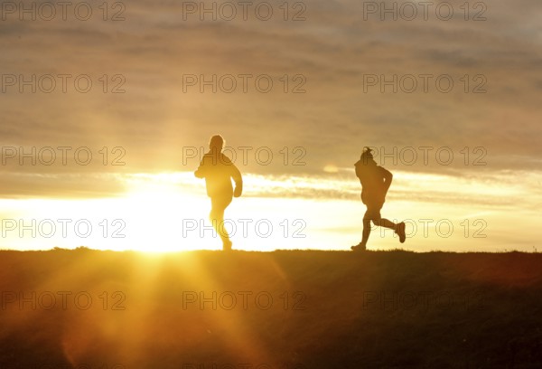 Woman and child walk across a dike on the island of Fehmarn at sunset, 13.10.2025, Fehmarn,