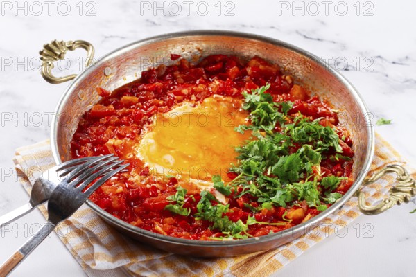 Traditional Turkish dish, scrambled eggs with tomatoes, Menemen, with herbs, in a frying pan,