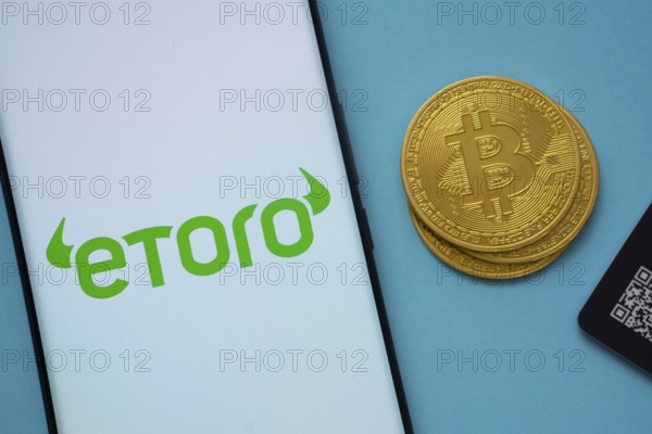 Dhaka, Bangladesh- 22 June 2025: eToro logo on smartphone screen near Bitcoin coin and QR code on