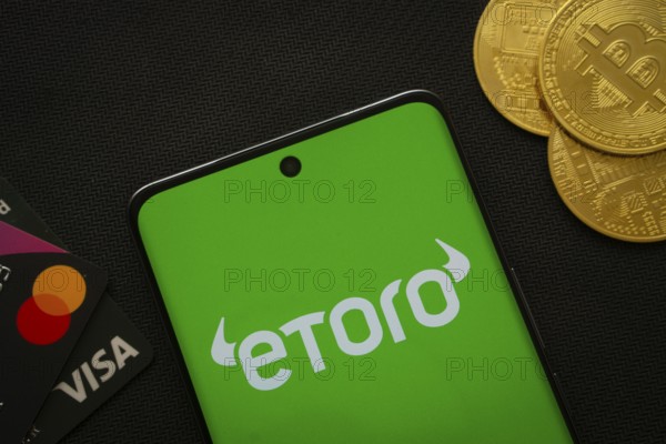 Dhaka, Bangladesh- 15 July 2025: Smartphone displaying eToro logo surrounded by Bitcoin coins and