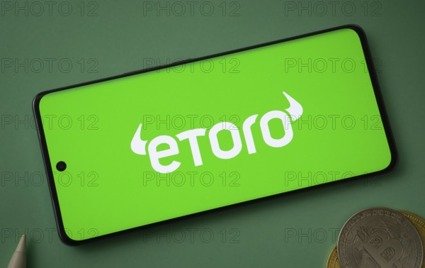 Dhaka, bangladesh- 12 June 2025: eToro logo displayed on a smartphone with Bitcoin coins on a green