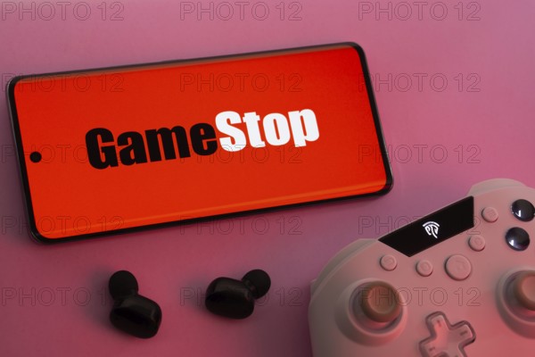 Dhaka, Bangladesh- 15 July 2025: Smartphone with GameStop logo, game controller, and earbuds on a