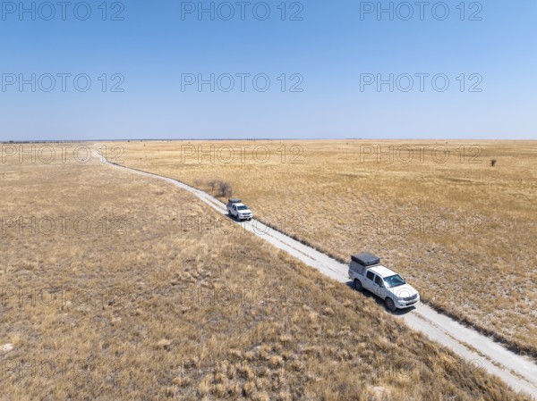 Two off-road vehicles drive on a sandy track through a vast dry landscape with yellow grass, Sowa