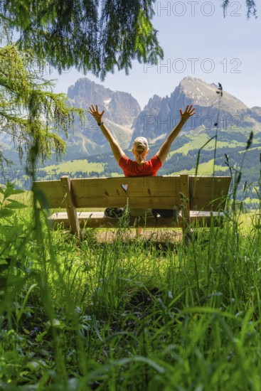 Person on a bench with outstretched arms in front of a mountain landscape, Alpe di Siusi,