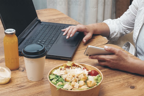 A woman is working on a laptop at home, there is food on the table, salad, coffee and juice,