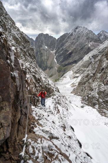 Mountaineer on a rope-secured path in a steep rocky mountain landscape with fresh snow in summer,