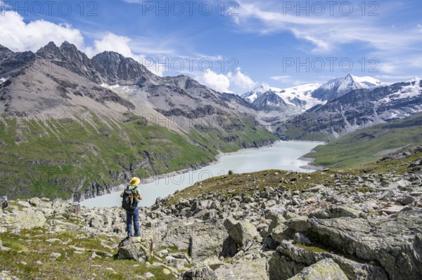 Mountaineer on a hiking trail at a blue mountain lake, reservoir Lac des Dix, behind mountain peak