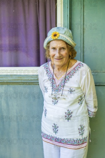 Portrait of a cheerful senior woman wearing a denim hat with a decorative sunflower, standing in