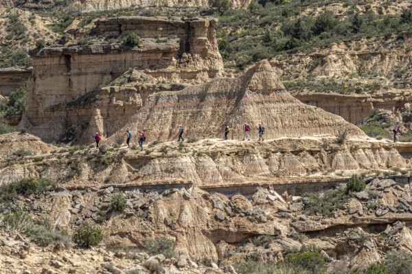 Group of hikers at colorful sandstone rock formations, desert, along gravel road Ruta Jubierre,