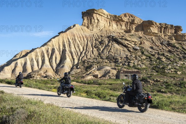 Biker riding motorcycle, gravel road, colorful rock formation, semi-desert, Bardena Blanca area,