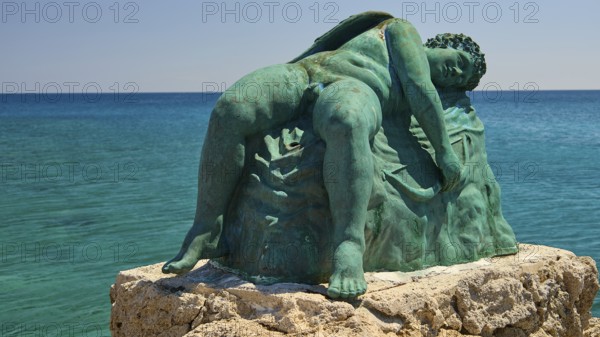 Bronze sculpture, sleeping Eros, close-up of an artistic statue on a rock by the blue water,