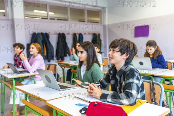 Elementary school students listening to the teacher and participating in the lesson using laptops