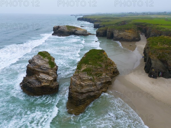 Gigantic, jagged rocks jutting out of the sea and lapped by foaming water, aerial view, Praia das