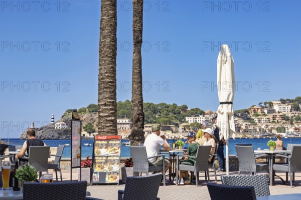 People sitting on a restaurant by the sea at a coast village at a tourist resort, Port de Sóller,