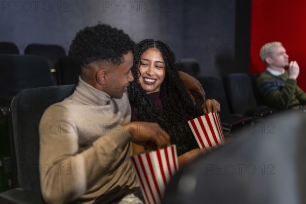 Happy couple enjoying a film in a cozy movie theater, sharing popcorn and laughing together,