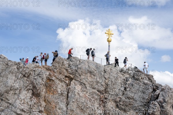 Many tourists at the summit of the Zugspitze with golden summit cross, overtourism, Wetterstein