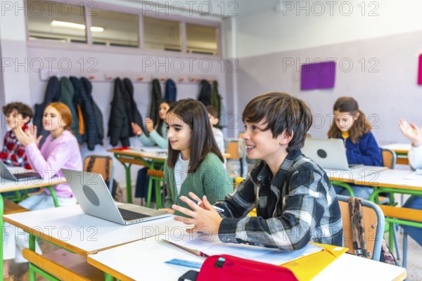 Elementary school students participating in an interactive lesson, raising hands and using laptops