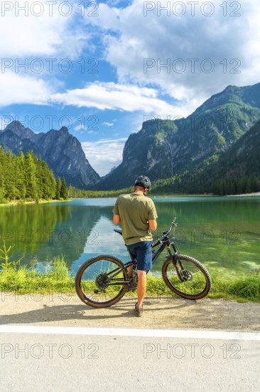 Mountain biker enjoying the breathtaking view of lake dobbiaco and the surrounding dolomites peaks