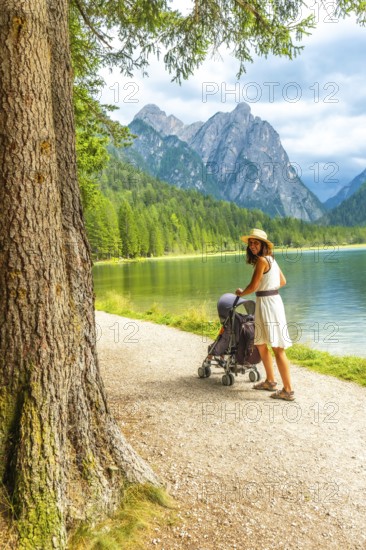 Tourist enjoying a walk with a baby stroller along the scenic shores of lake dobbiaco, surrounded