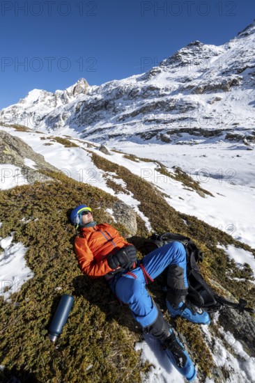 Ski tourer taking a break in the sun, lying down, taking a nap, snowy mountain landscape in winter,