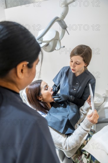 Dentist examining patient's teeth with dental tools while a nurse assists in a bright, modern