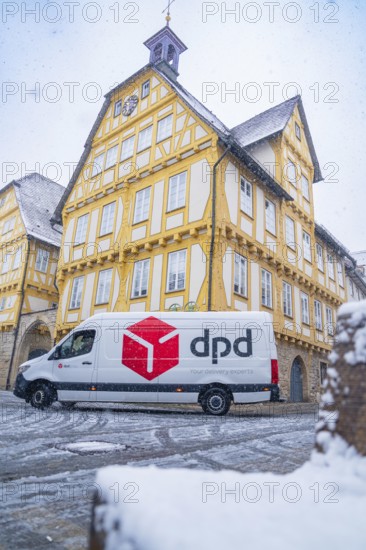 A DPD delivery van stands in front of a yellow-painted half-timbered building covered in snow,