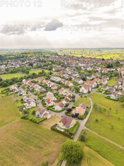 Residential area with densely built houses and streets, surrounded by fields under a slightly