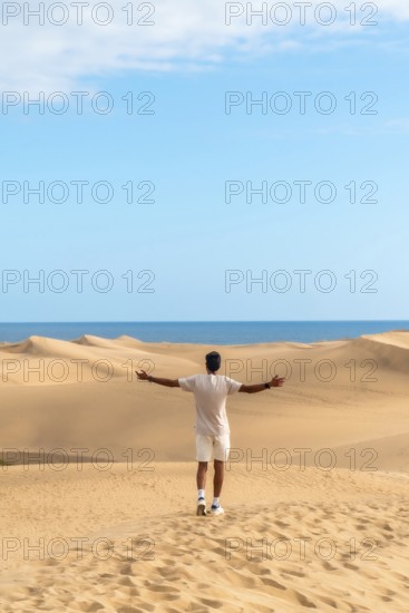 Young man opening arms in maspalomas dunes, gran canaria, feeling freedom and enjoying the desert