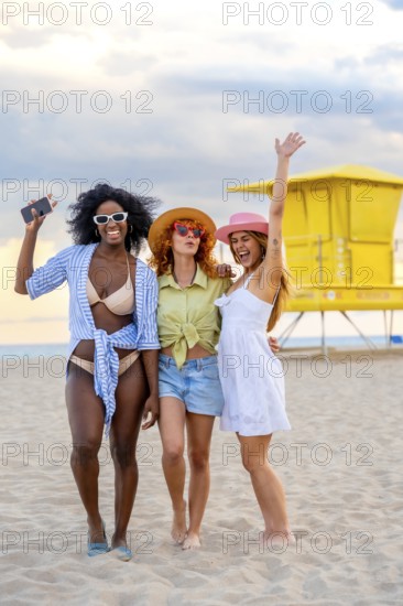Three cheerful multiracial young women enjoying summer holidays on miami beach, laughing together