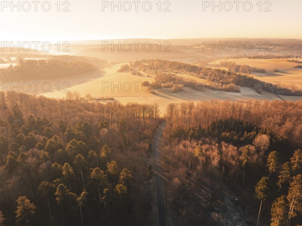 Aerial view of a road through a forest and past fields in the soft morning light, Gechingen