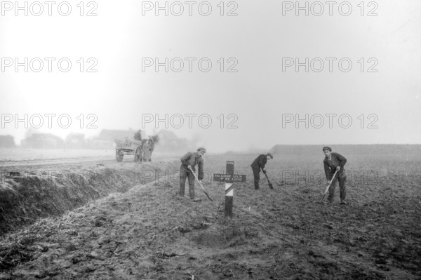 Wooden cross on grave of fallen soldier and workers levelling field on former battlefield after the