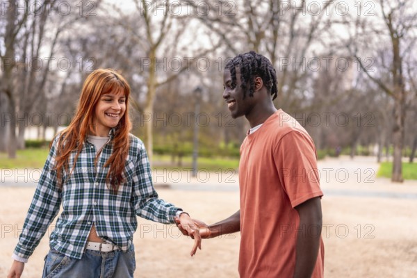 Young interracial couple holding hands and smiling while walking in a park, enjoying a romantic