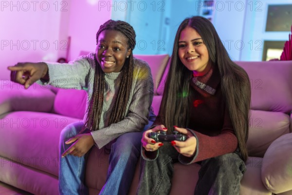 Two friends enjoying their free time playing video games at home, sitting on a comfortable sofa in