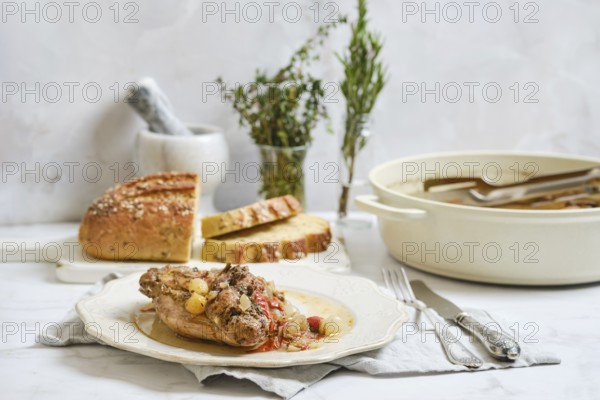 Cooked rabbit stew is served on a plate with herbs on top. Fresh bread is placed next to the dish